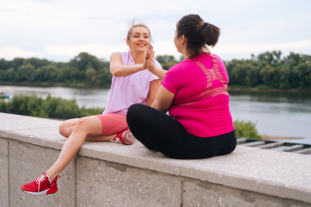 快乐的专业健身女教练和积极超重的年轻女性在户外锻炼后互相问候与击掌。图片下载
