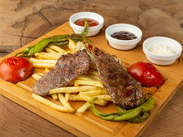 炸薯条、肉丸、辣椒、西红柿和酱汁放在木头上的黑色盘子上图片下载