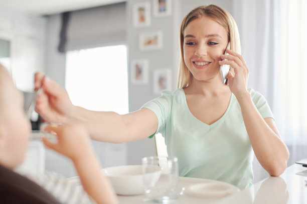 年轻的母亲一边用勺子喂孩子，一边讲电话图片下载