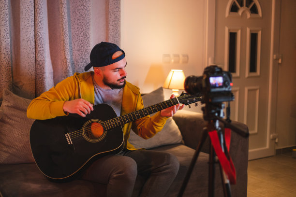 留着大胡子的年轻音乐老师，一边在家里弹吉他，一边用单反相机为YouTube录制教程图片下载