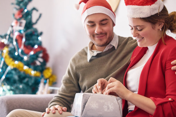 这张照片拍摄的是一对快乐的年轻夫妇在圣诞节期间在家打开礼物图片下载