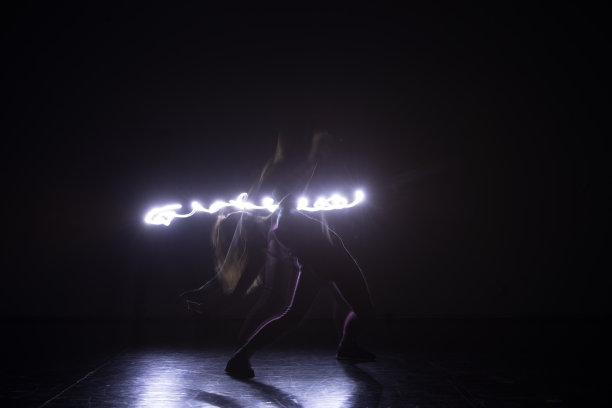 现代艺术舞者，在黑色背景和霓虹蓝色灯光下跳舞，同时伸展和扭动她的身体。图片下载