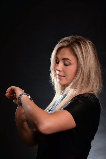 美丽的金发女孩看着黑色背景上的手表图片下载