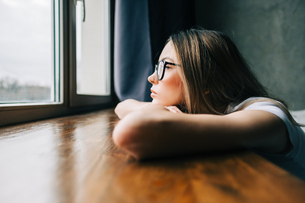 年轻无聊的千禧一代女人独自在家看着窗户。疲惫或情感枯竭的概念图片下载