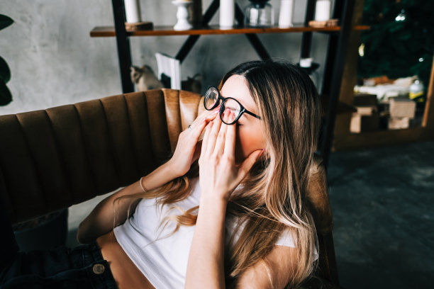 年轻女子戴上眼镜后揉揉眼睛。眼睛疼痛或疲劳的概念。图片下载