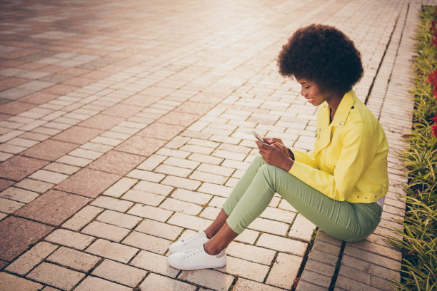 在公园里，一名女子双手拿着手机，坐在花束环绕的路边发短信图片下载