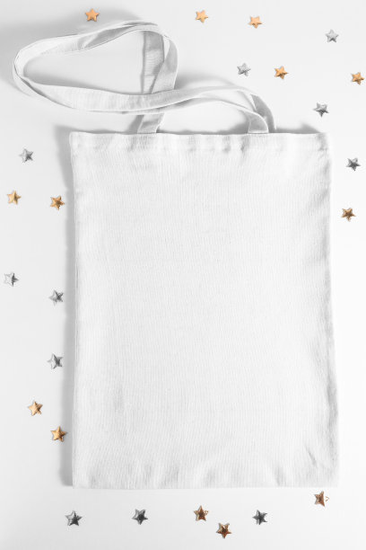 一个白色纺织袋的模型在木制的桌子上与金色的星形纸屑顶部视图。带有复制空间的空模板。图片下载