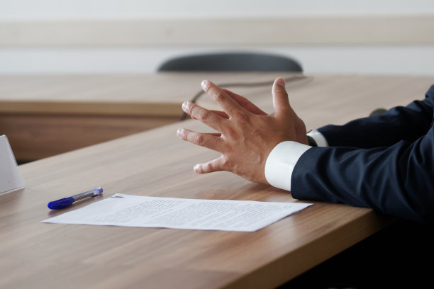 一个穿着优雅西装的男人的手放在一张木桌上，旁边是一张纸和一支笔。匿名与会者、官员、老板、律师或商人。没有一张脸图片下载