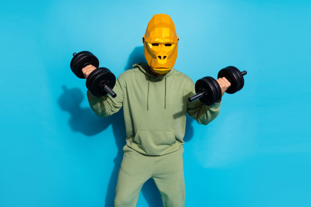 照片中酷酷的古怪男人戴着灵长类动物面具，举起两个哑铃，孤立的蓝色背景图片下载