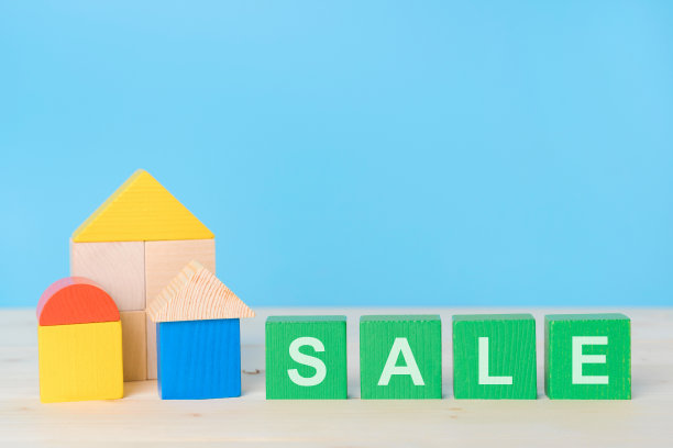 绿色木块上的“SALE”字样，蓝色背景上的木头立方体房子。销售房地产的概念图片下载