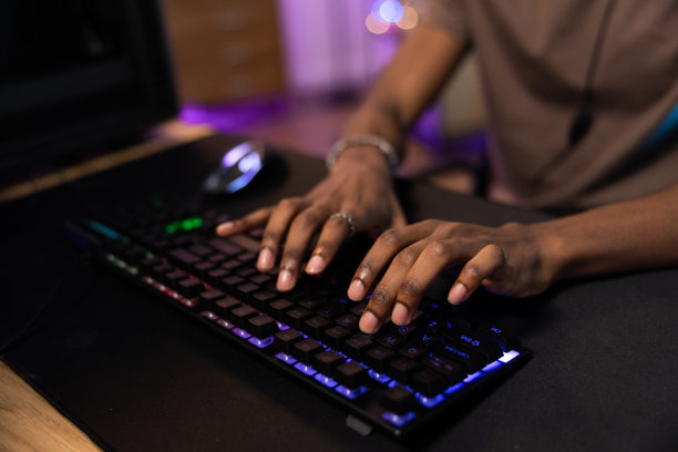 一个男性玩家按下专业彩色背光键盘上的按钮，led灯，在电脑上玩游戏的特写镜头图片下载