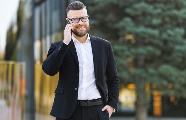 年轻快乐的商人戴着眼镜，在阳光明媚的日子里走在外面，和亲密的朋友或家人用手机聊天，享受着上班路上的愉快交谈图片下载