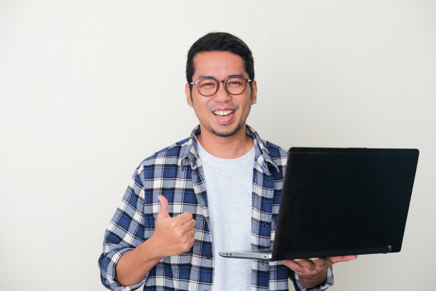 成年亚洲人微笑快乐，给大拇指，而持有笔记本电脑图片下载