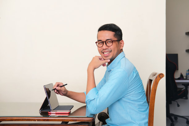 成年亚洲男子微笑自信，而使用移动平板电脑工作图片下载
