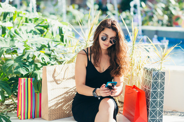 一个年轻漂亮的女人叫了一辆出租车到商场，打电话，谈论她在商场里买的东西，喜欢购物和新衣服。微笑图片下载
