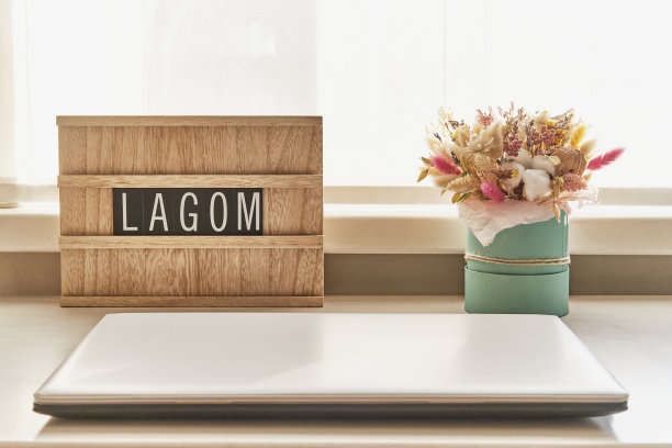 在笔记本电脑旁边的白色桌子上，有一束漂亮的干花和木制的标识，上面写着LAGOM图片下载