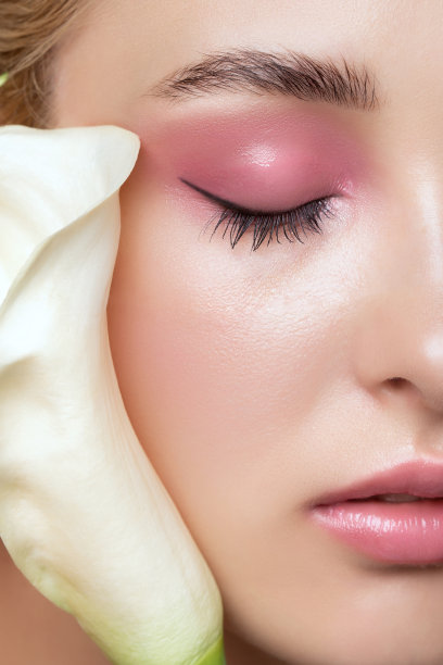 金色头发的美丽女孩的肖像，美丽的创意粉红色化妆品和健康清洁的皮肤。她的脸旁边有一朵美丽的花。化妆美容概念。图片下载