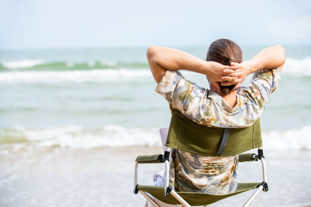 白人商人坐在户外的椅子上，在海滩上用笔记本电脑工作。图片下载