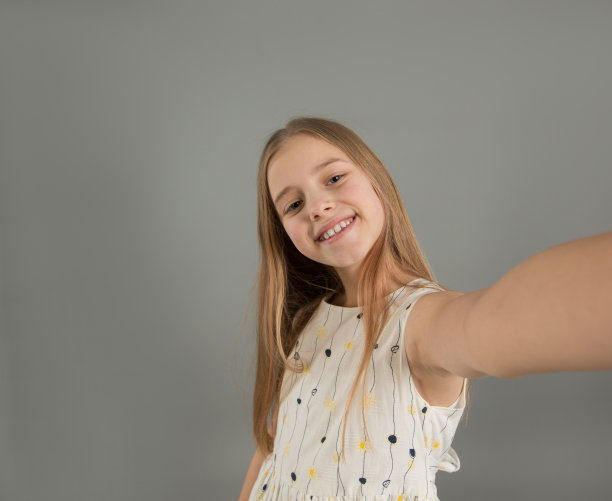 一个有趣的年轻女孩的自拍照与她的手臂伸出孤立的灰色背景图片下载