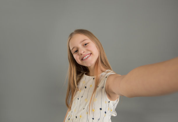 一个有趣的年轻女孩的自拍照与她的手臂伸出孤立的灰色背景图片下载