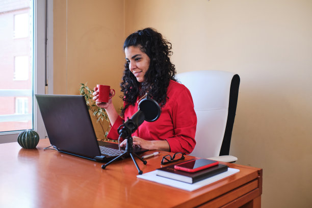 西班牙裔女性，一杯热饮，带着笔记本电脑和麦克风在家工作图片下载