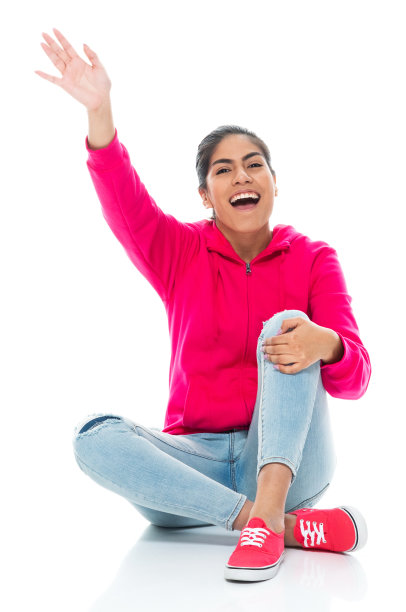 z一代年轻女性穿着牛仔裤坐在白色背景前面的地板上图片下载