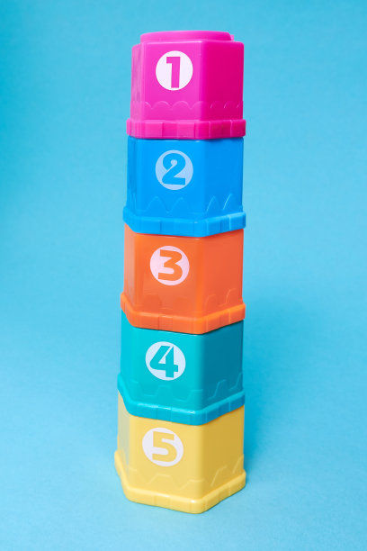 蓝色背景上的儿童彩色塑料玩具金字塔排成一排。儿童金字塔用字母和数字表示儿童的发展。副本的空间。图片下载