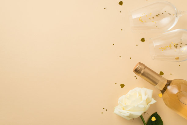 俯视图照片白玫瑰两个葡萄酒杯与金色亮片心形纸屑和瓶白葡萄酒在孤立的米色背景与空空间图片下载