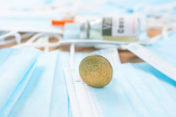 一枚硬币和医用口罩的特写照片，背景为医用玻璃小瓶和塑料注射器。图片下载