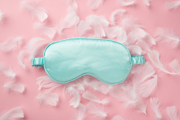 蓝色丝绸睡眠面具和羽毛的俯视图照片在孤立的粉彩粉红色背景与空白空间图片下载