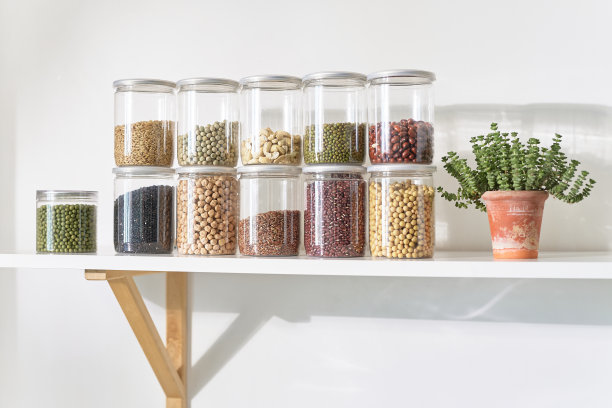 在明亮的室内厨房架子上，整齐排列的玻璃罐里装满了各种豆类和全谷物。图片下载