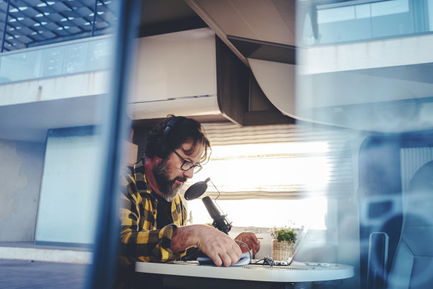 一个人在露营车里用麦克风做播客演讲。游牧网络是现代人的生活方式。替代办公室和智能工作技术。旅行和工作职业，成年男性，自由职业者图片下载