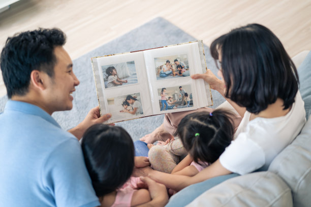 亚洲家庭看着旧相册上的照片回忆过去。年轻漂亮的夫妇和年幼的女儿坐在一起，翻动着相册，享受着回忆彼此关系的时光。图片下载