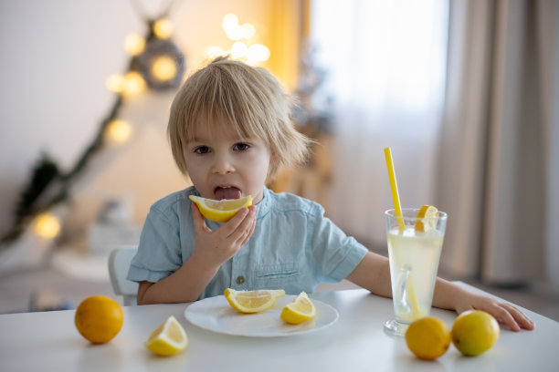 可爱的蹒跚学步的孩子，金发男孩，在家舔柠檬喝柠檬水图片下载