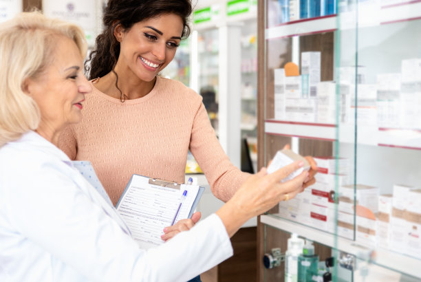 高级药剂师在药店向年轻女性顾客销售药品。图片下载