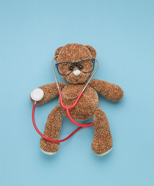 一个带眼镜的针织泰迪熊，蓝色背景上的红色听诊器。图片下载