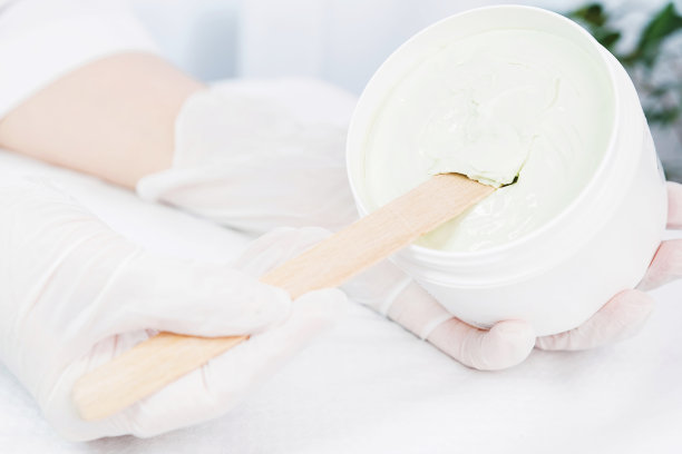 近距离照片的美容师手在医疗手套，持有一罐奶油产品刮擦，并试图把它从罐子在美容师橱柜。图片下载