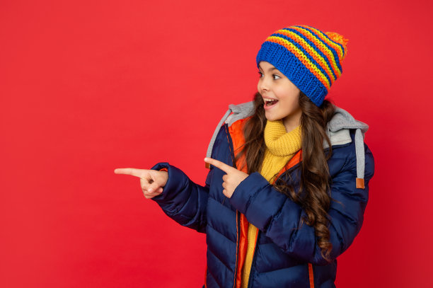 惊奇的孩子在针织的冬季帽和羽绒服点手指复印空间，广告图片下载