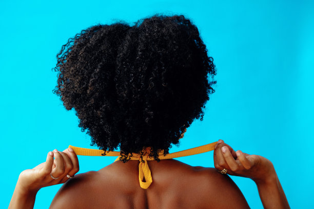 年轻的成年妇女与卷曲的头发与系泳衣的背部镜头图片下载