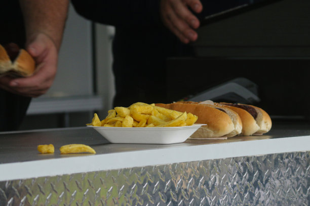 照片中，一群不知名的小贩在餐车柜台后面供应快餐外卖，用一次性聚苯乙烯盘子盛着薯条，用面包包着两个热狗香肠图片下载