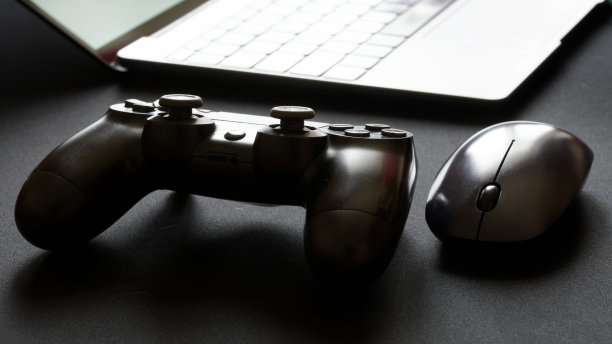 一个视频游戏操纵杆和一个电脑鼠标放在一个打开的超薄笔记本电脑旁边。背光和轮廓。专业的游戏概念图片下载