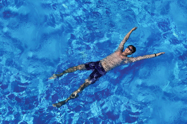 年轻的白人男子漂浮在蓝色的水在游泳池。前视图。暑假，休闲，度假旅游图片下载