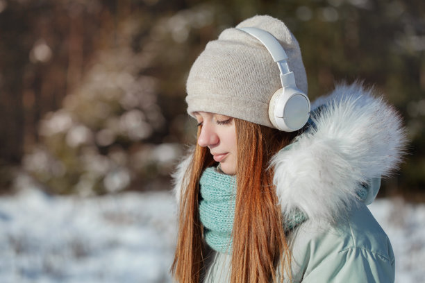 照片上的快乐的年轻女孩微笑着带着耳机在冬季公园，闭着眼睛在梦中，完全平静图片下载
