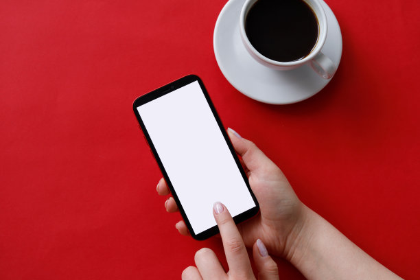 在红色背景下，一个女人一手拿着手机，另一只手拿着一杯咖啡的俯视图。图片下载