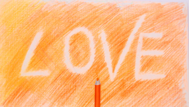 橙色背景上的铭文。彩色铅笔背景。题词是爱。一支橙色的小铅笔图片下载