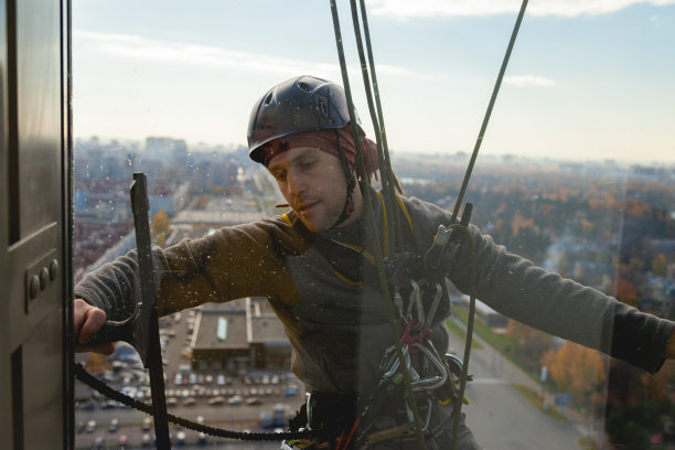 戴着头盔的工业攀爬者在一幢多层建筑的公寓里清洗窗户图片下载