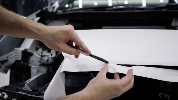 详细的车。师傅用小刀在机器上切胶卷。在汽车上涂上一层白色的保护膜后，大师用小刀在保护膜上划了一个口子，以保护汽车免受划痕和碎片的伤害图片下载