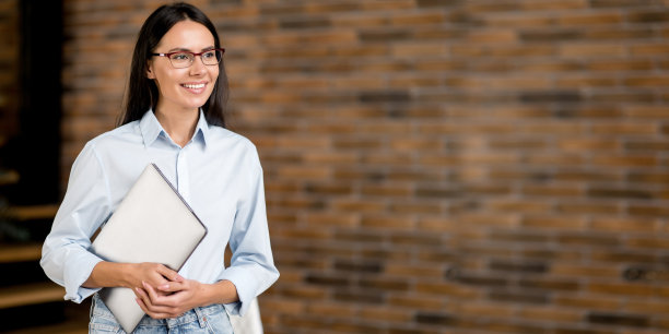 肖像自信成功聪明漂亮的白种人女人。女办公室经理、教师、财务导师，站在办公室里，手里拿着笔记本电脑，目光移开，微笑友好。复制空间,空墙图片下载