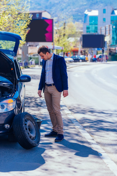 一位身着蓝色西装的绅士正把车停在一条繁忙的林荫大道上换轮胎。图片下载