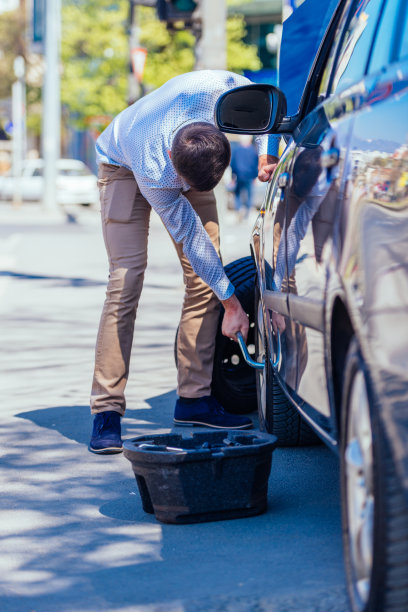 在一个阳光明媚的日子里，一位满身是汗、疲惫不堪的年轻企业家在换车胎时擦着额头上的汗水图片下载